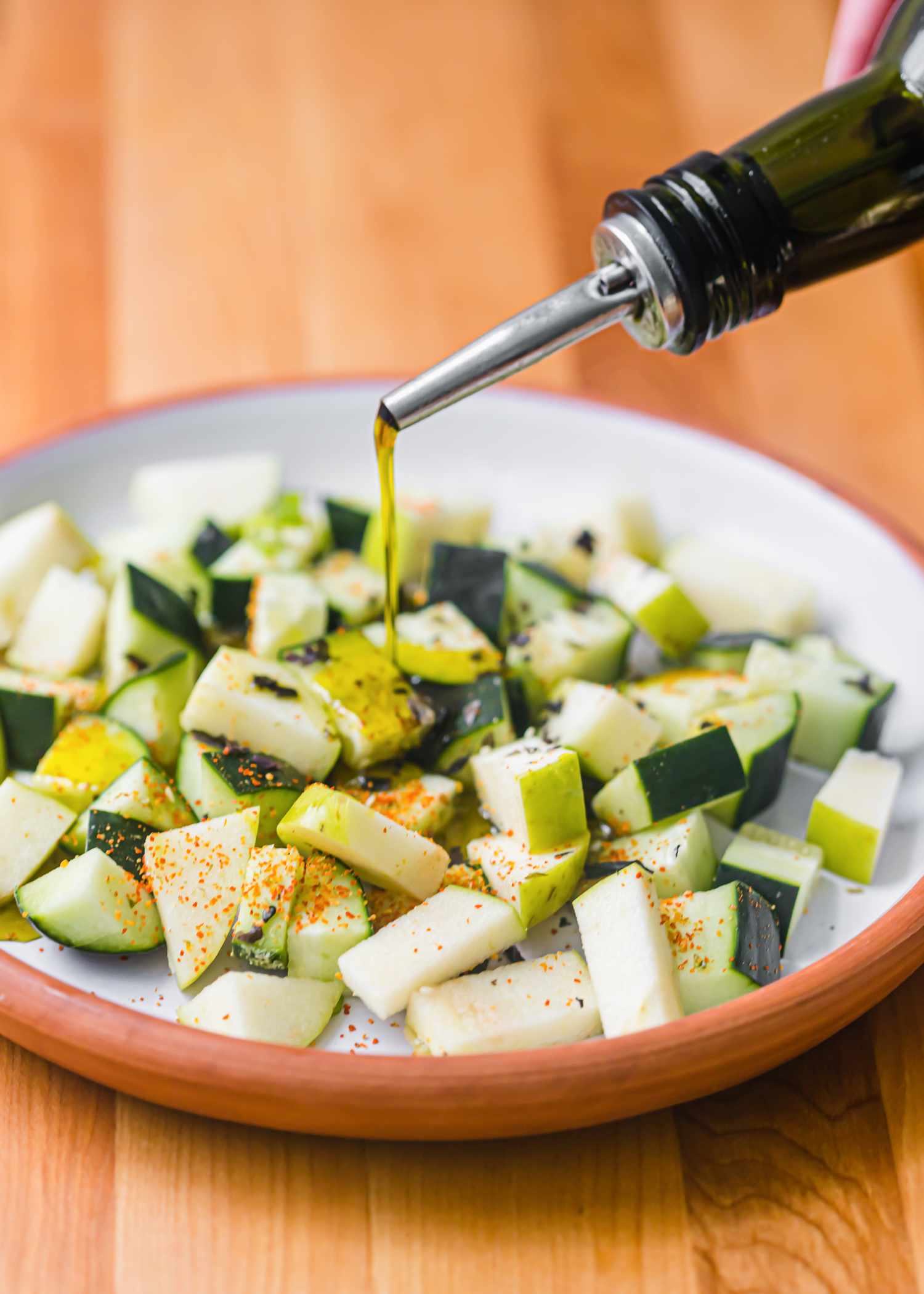 Pouring avocado oil on a bowl of chopped cucumber