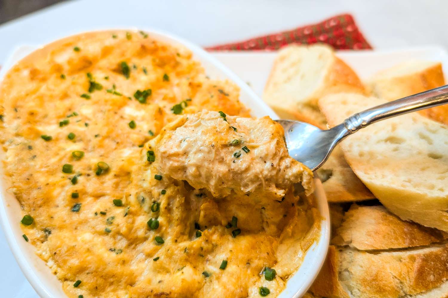New Year’s Eve Hot Crab Dip in a dish with a spoon scooping some out, slices of bread on the side