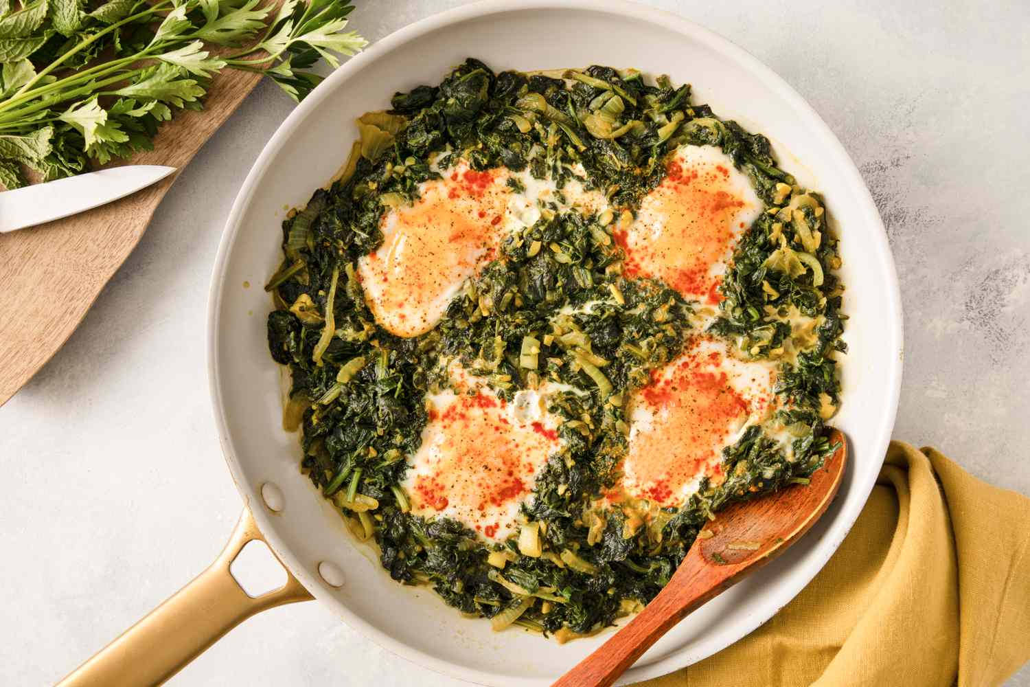 A pan of Nargesi a Persian dish with eggs cooked atop seasoned sauted greens displayed on a countertop next to utensils