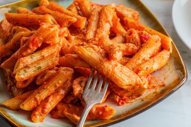 A plate of penne pasta in a creamy tomato sauce with a fork
