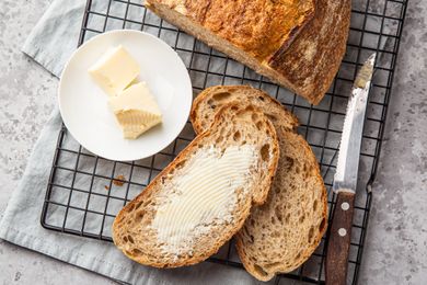Slices of bread with butter on a cooling rack accompanied by a plate with butter and a knife