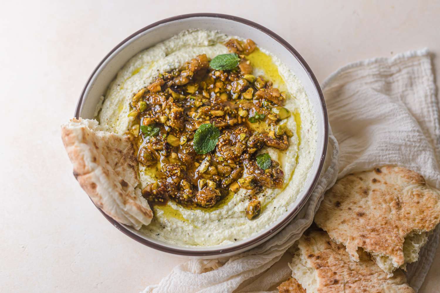 Whipped feta with figs, nuts, and honey in a bowl with bread dipped in the side.