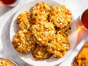 A plate of apple cheddar oat cookies surrounded by glasses of a beverage on a table
