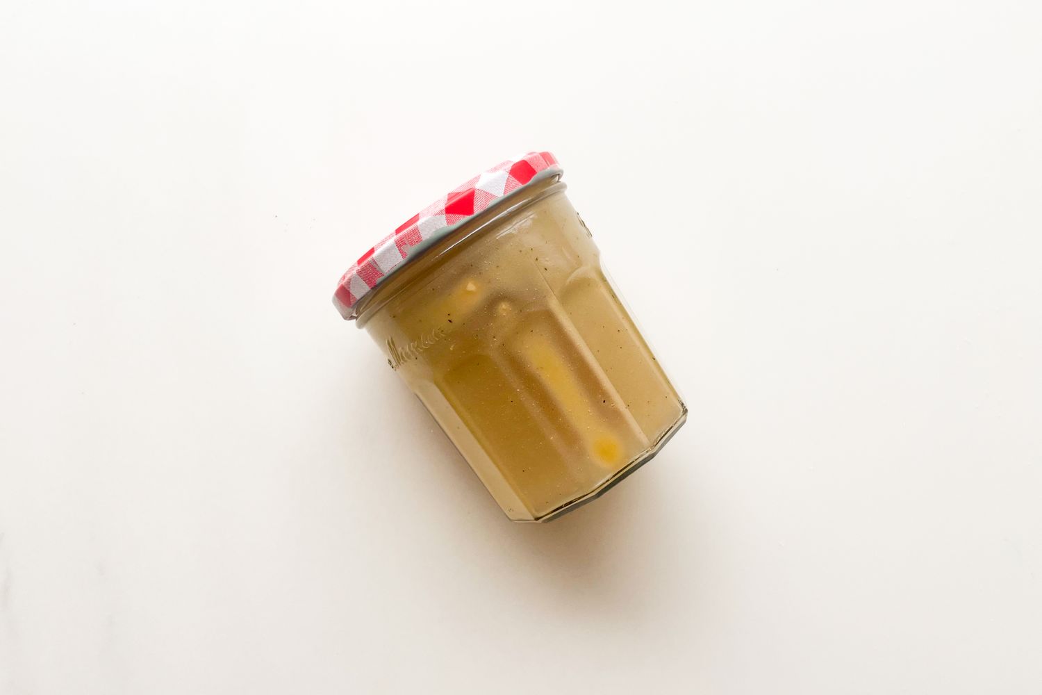 A jar with a red and white checkered lid containing salad dressing