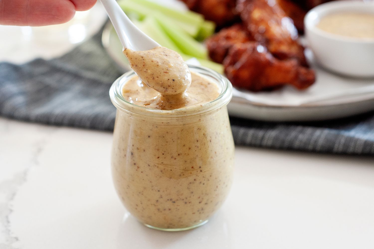 Spooning honey mustard sauce out of a glass jar.