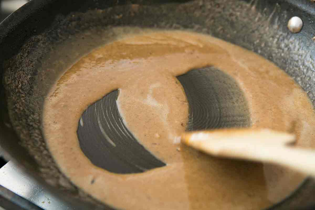 Country fried sirloin gravy from drippings being stirred with a wooden spoon 