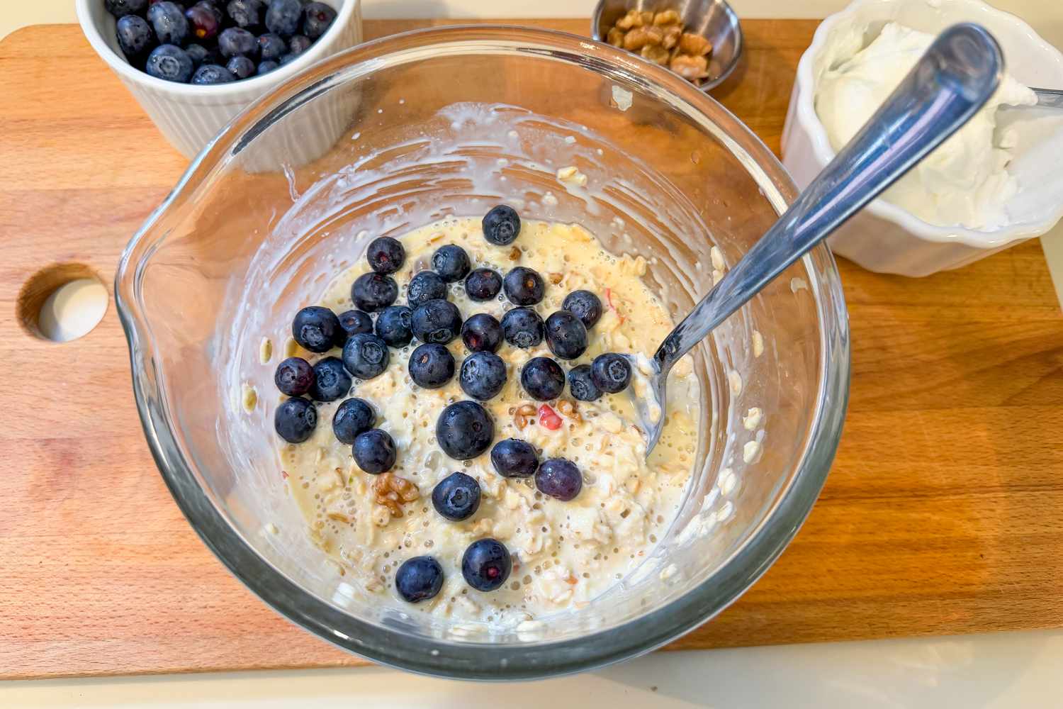 A bowl of oatmeal topped with blueberries on a wooden cutting board with additional ingredients nearby