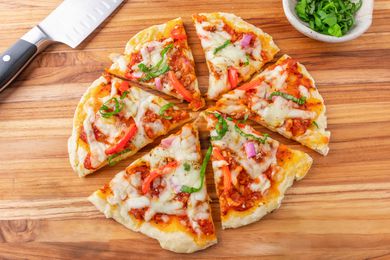 homemade pizza on a wooden counter next to a bowl of chopped basil and a knife
