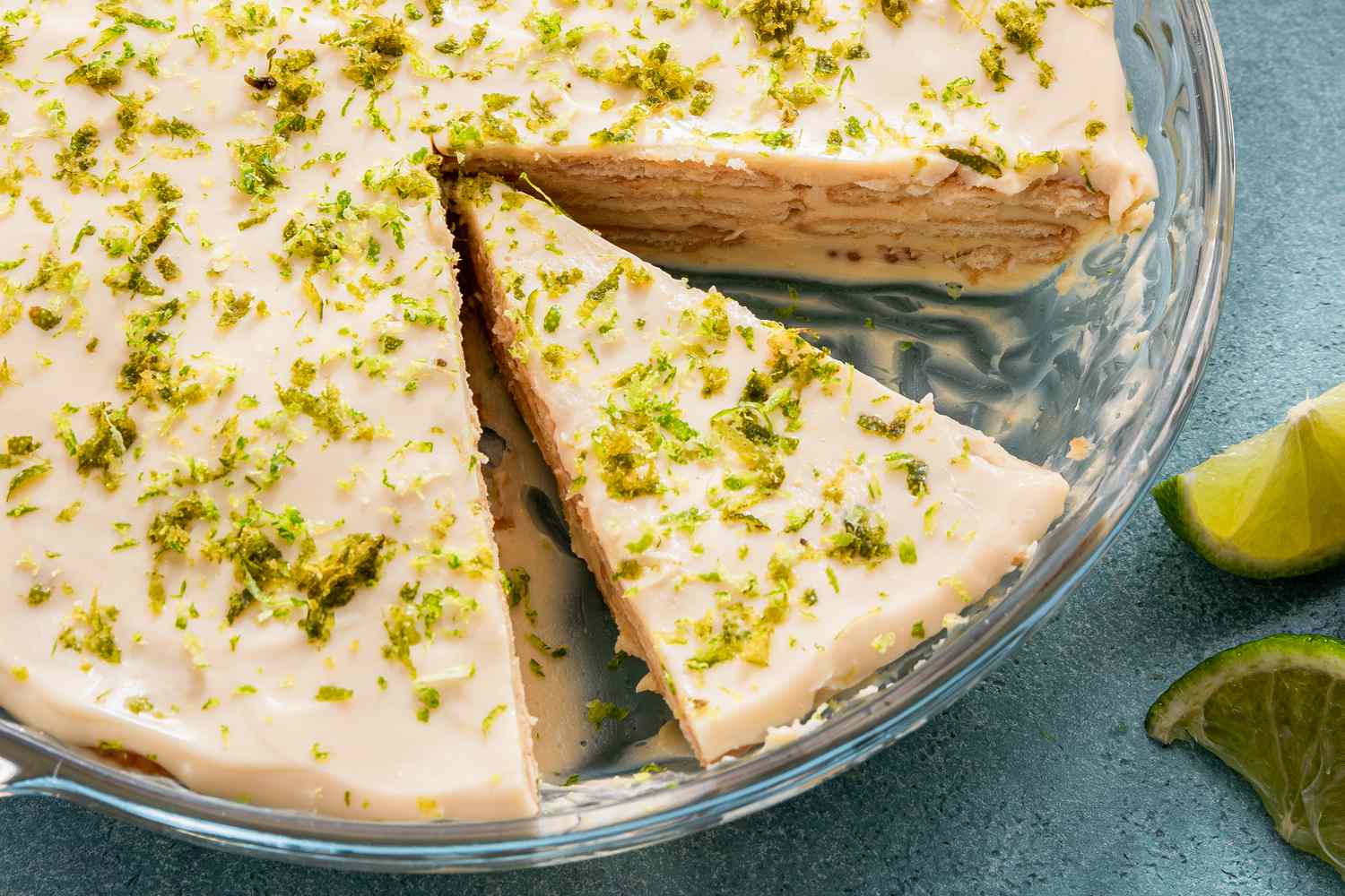 A no-bake lime dessert in a glass baking dish with a slice cut out, garnished with lime zest