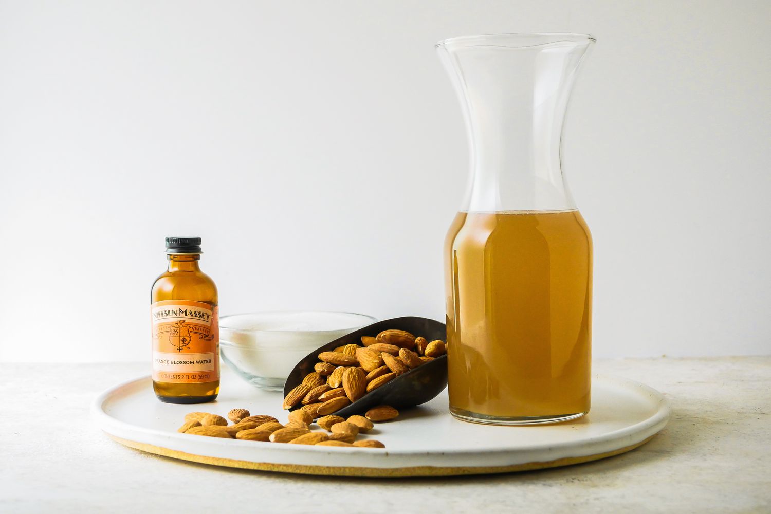 Quick and easy orgeat in a pitcher on a tray with a scoop filled with almonds and extract.