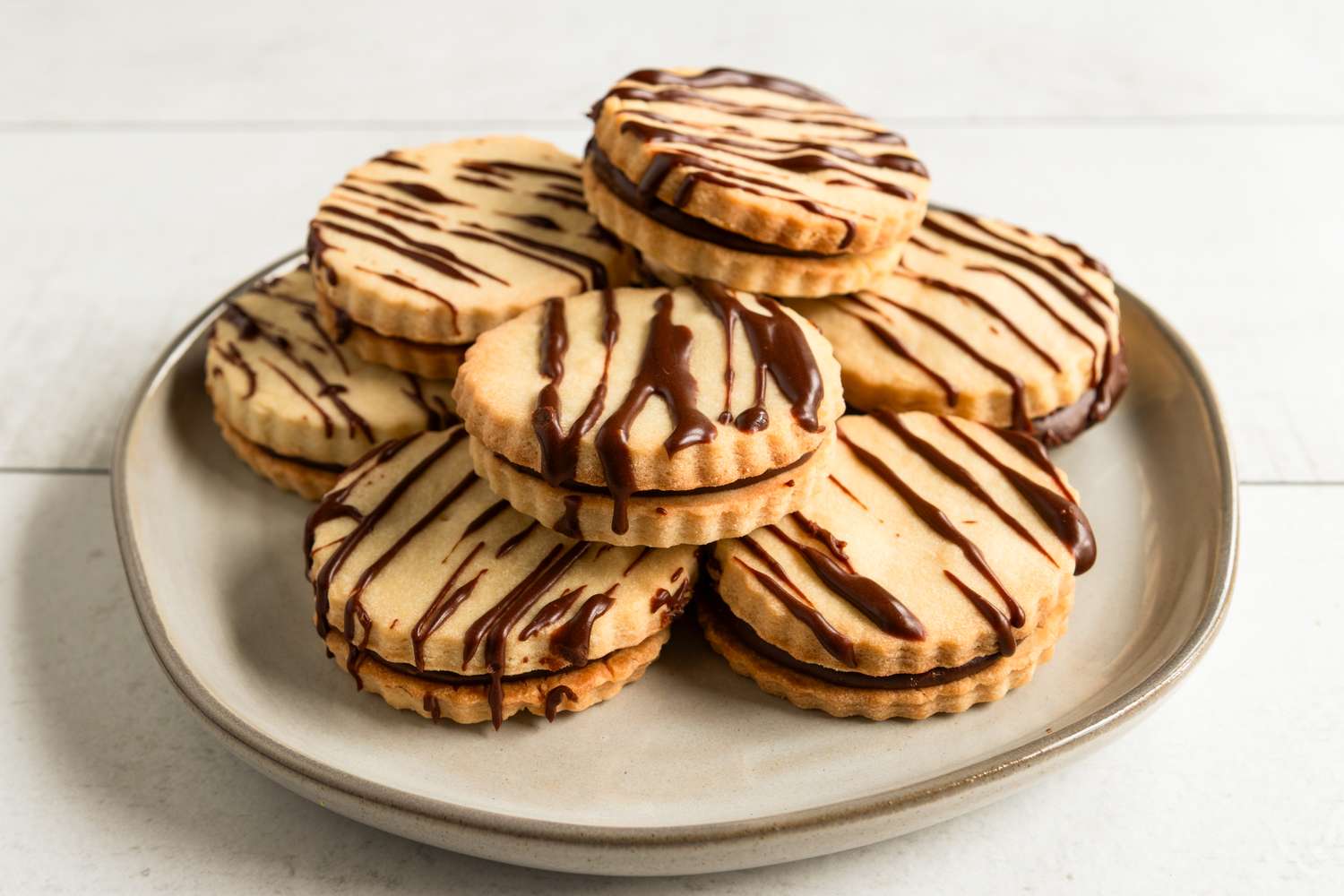 Stack of cookies on a plate topped with chocolate drizzle and filled with chocolate