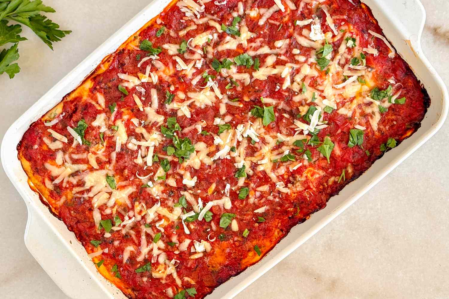A baked dish of lasagna topped with tomato sauce cheese and herbs on a countertop