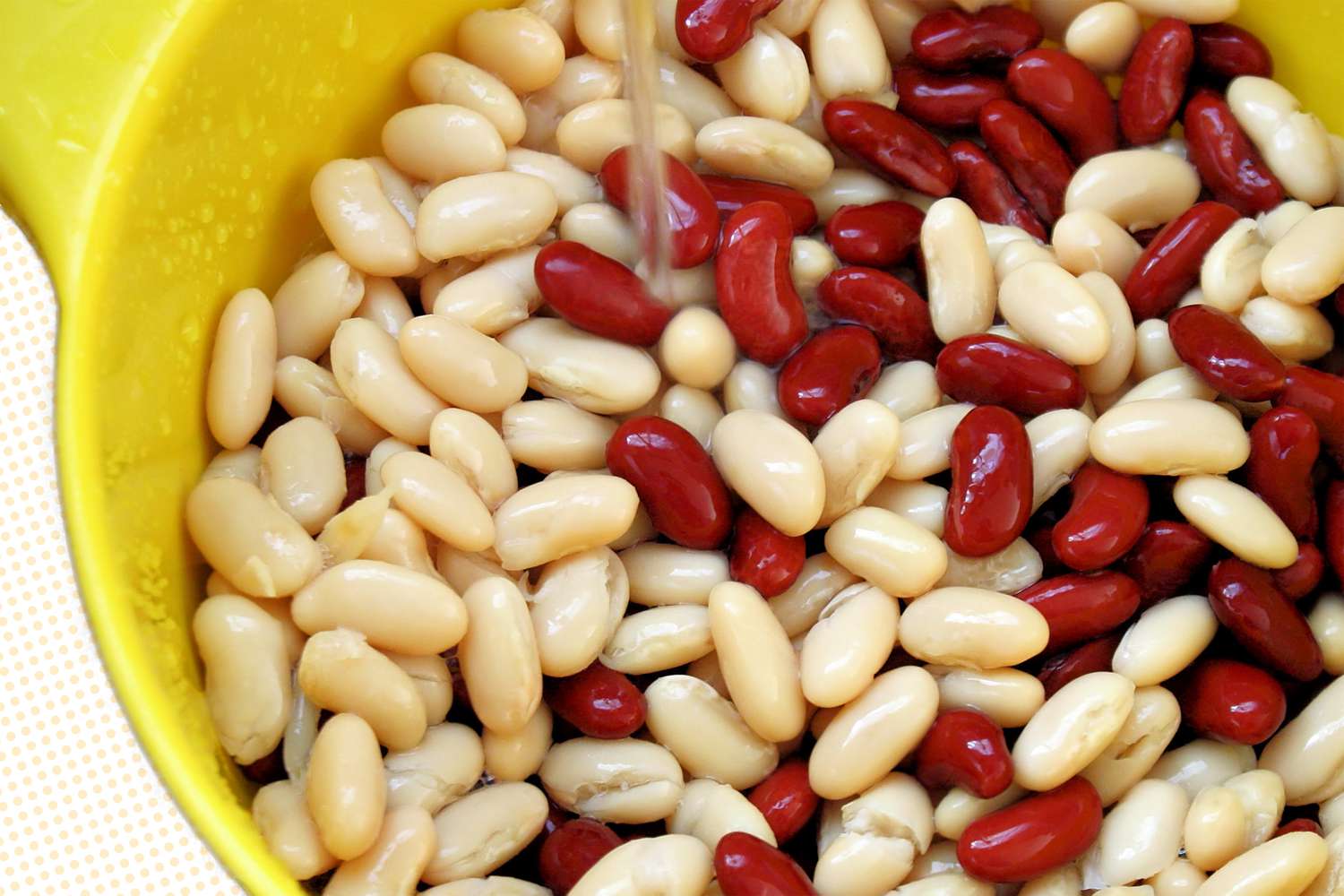 White and red beans in a yellow bowl with running water