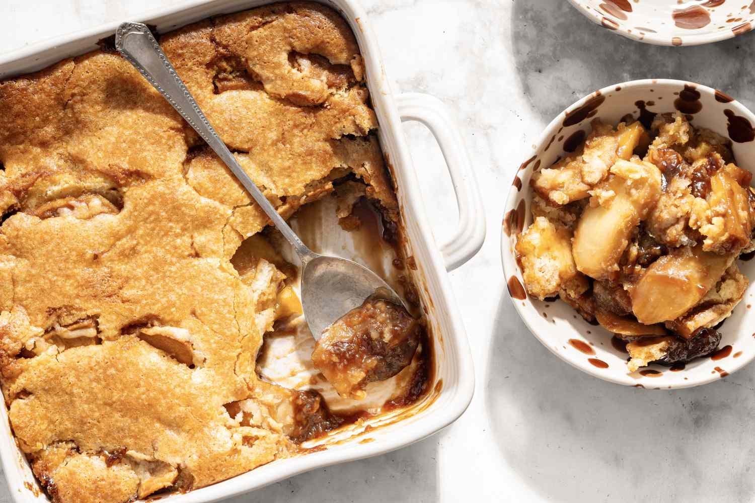 Caramel apple cobbler in a baking dish with a serving spoon and a portion served in a bowl