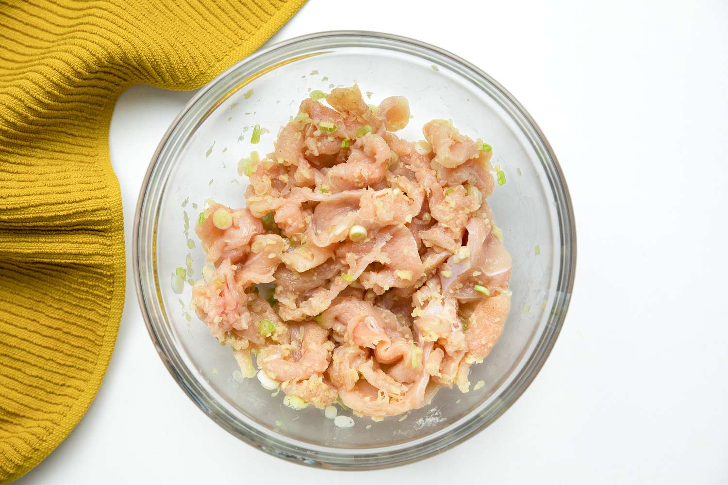 Bowl of Marinated Chicken Next to a Mustard Colored Kitchen Towel for Chicken Congee Recipe