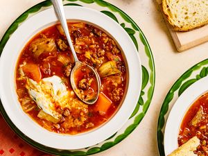 Cabbage roll soup served in a white bowl with a spoon garnished with sour cream surrounded by bread