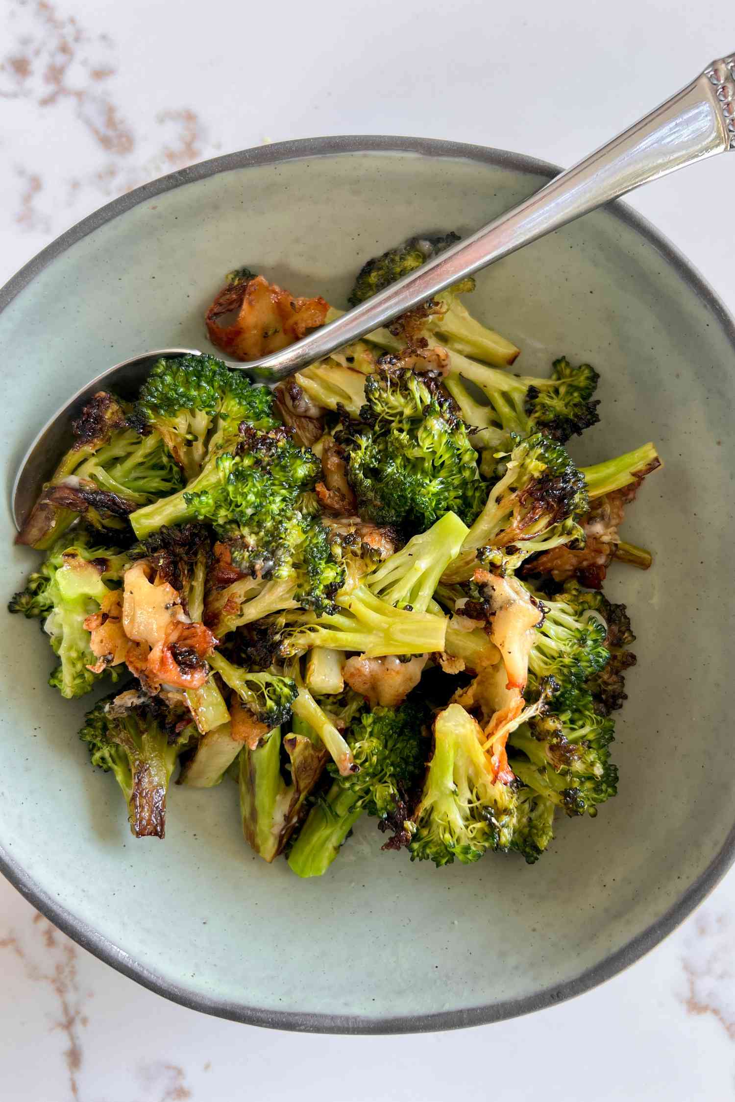 Cheesy broccoli in a neutral bowl and a spoon