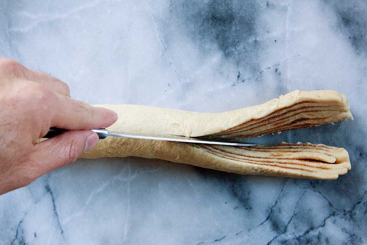 A knife is slicing the tube of King Cake dough down the middle.