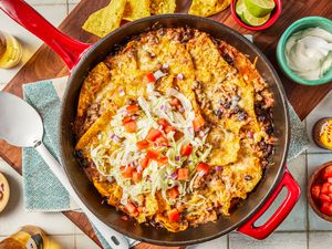 easy taco casserol in a pot at a table setting with bowls of toppings, chips on a platter, and a bottle of beer