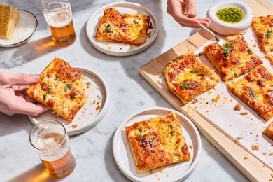 Square puff pastry pizza slices served on plates with drinks garnished with herbs and accompanied by a dipping sauce
