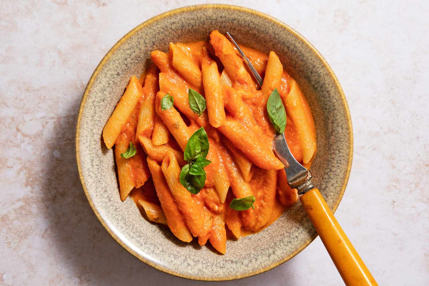Giada's penne alla vodka in a beige bowl with a fork, garnished with basil