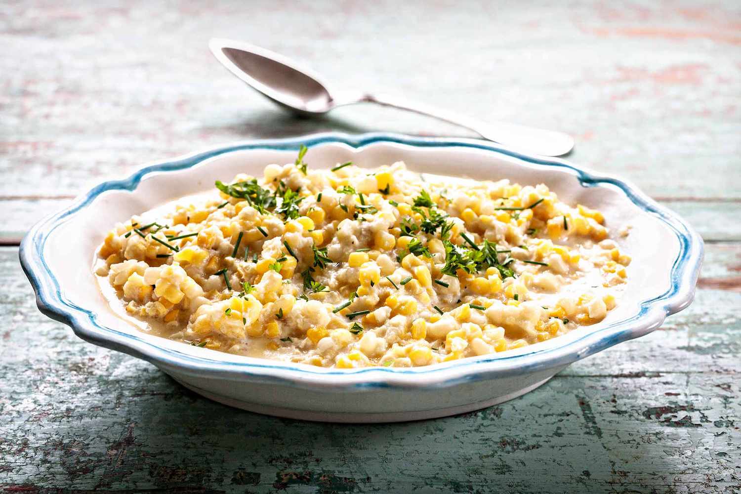 Best Creamed Corn Recipe - bowl of creamed corn wtih spoon and herbs