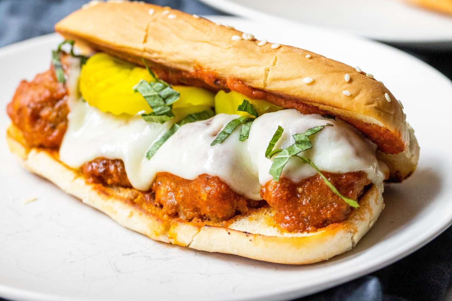 A Plate of Meatball Sub Topped with Banana Peppers and Basil 