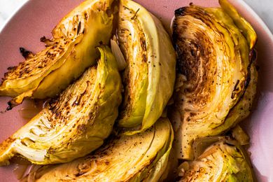 Overhead view of 6 wedges of melting cabbage on a pink plate