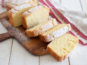 Slices of A slice of Olive Oil Yogurt Cake on a wooden paddle and dusted with powdered sugar.