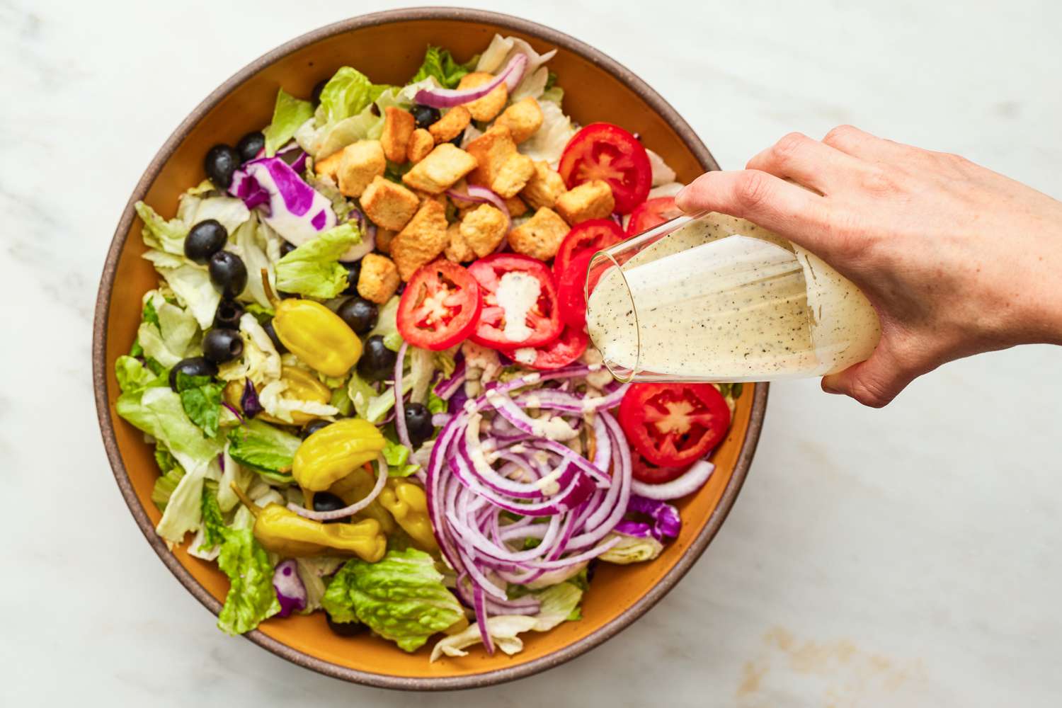 Glass of Salad Dressing Poured Over a Bowl of Copycat Olive Garden Salad Recipe
