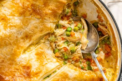 A pot pie in a baking dish partially served with a metal spoon
