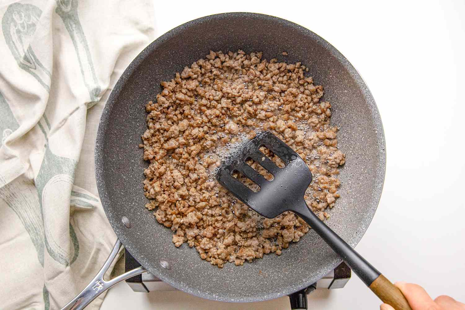 Ground Pork Stirred Using a Slotted Spatula in a Pan on a Portable Burner Next to a White Kitchen Towel for Mapo Tofu Recipe