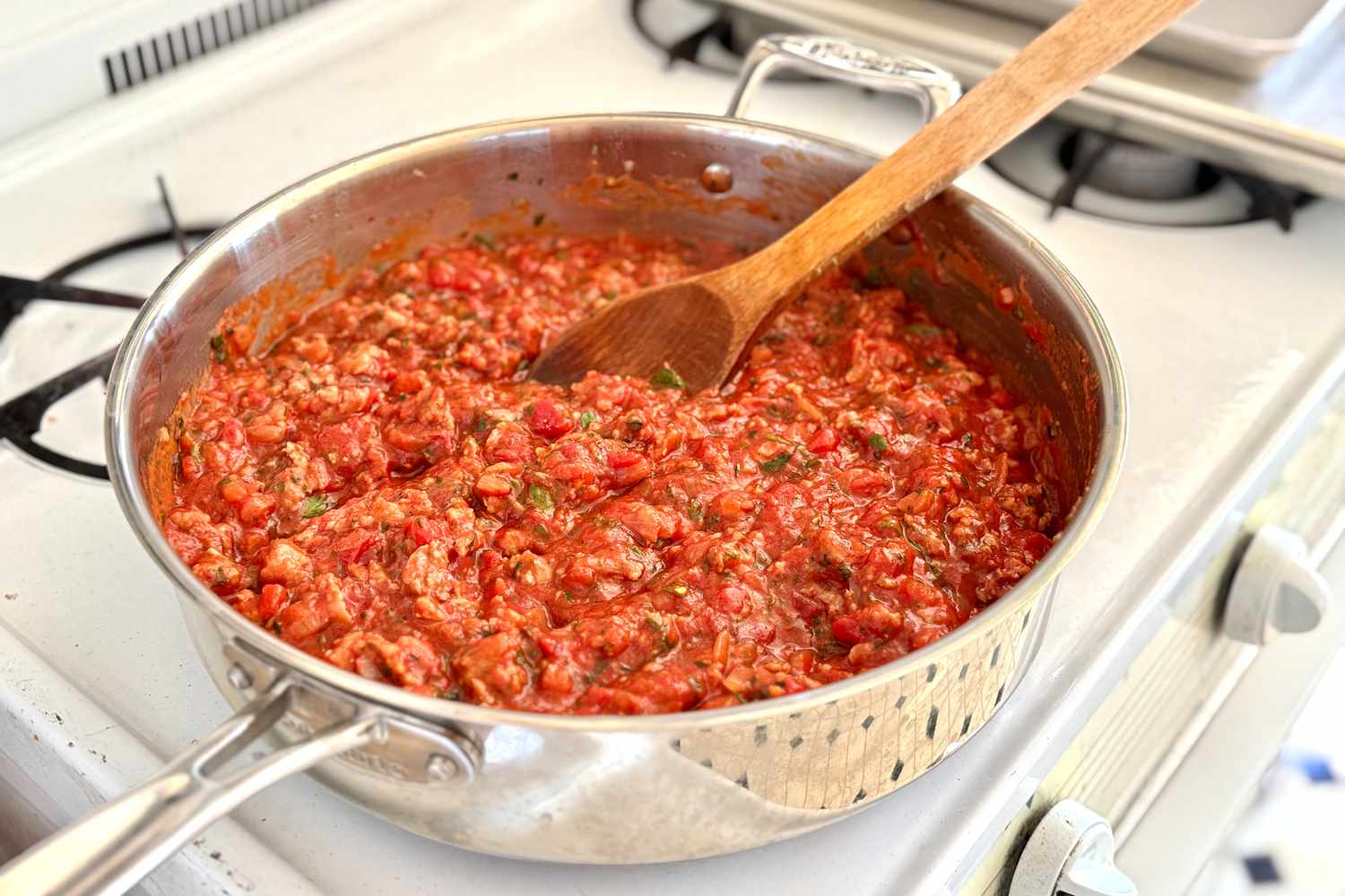 A saucepan with lasagna meat sauce on a stove stirring spoon placed in the mixture