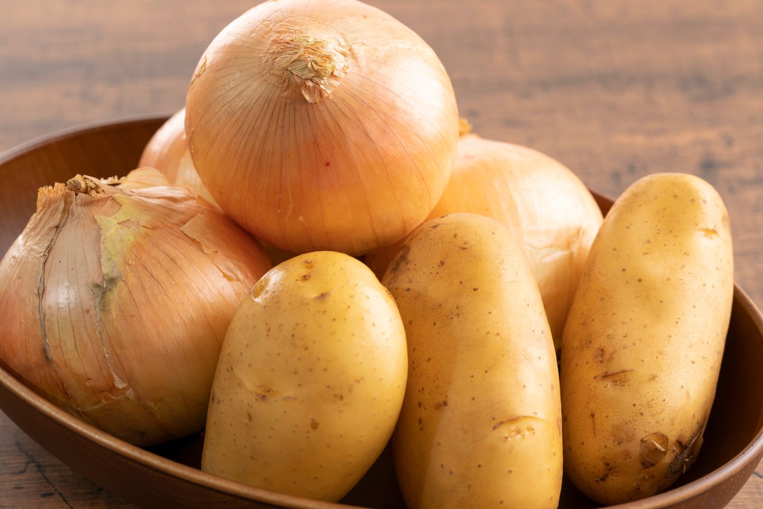 A bowl containing whole onions and potatoes