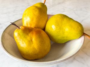 Three delicious Bartlett pears in a bowl on a marble countertop