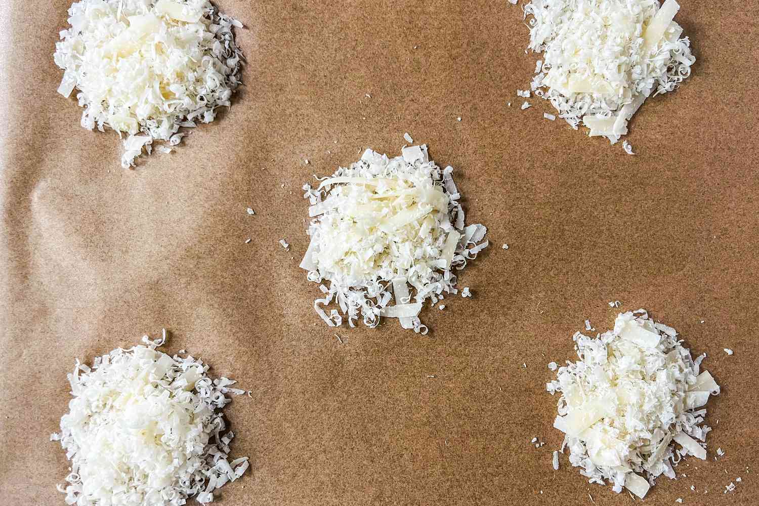 Mounds of shredded cheese on parchment paper, prepared for baking