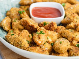 A serving tray with homemade chicken nuggets and ketchup on it.