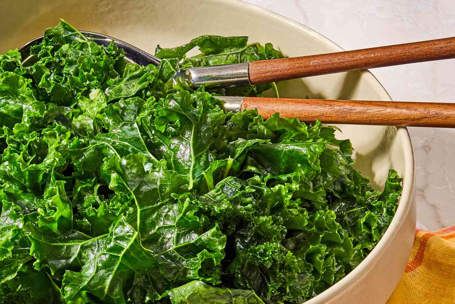 Closeup view of a large bowl of kale salad with serving spoons
