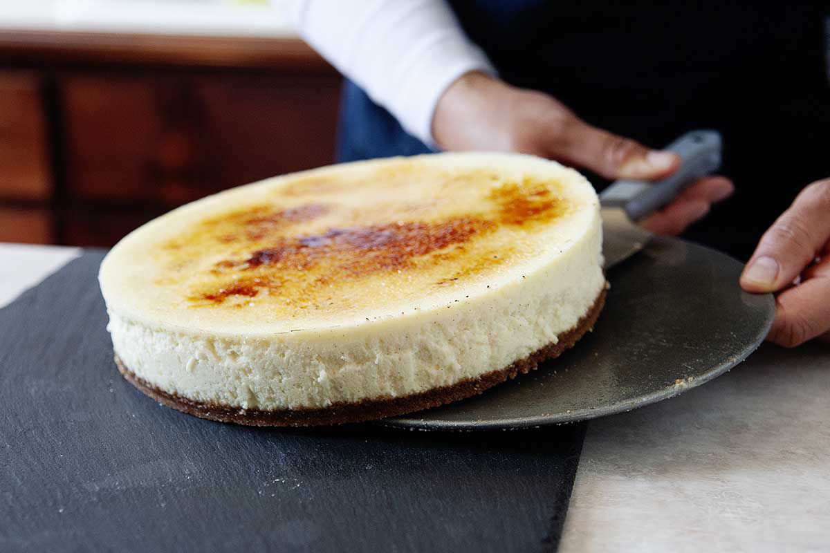 A woman transferring a Vanilla Bean Cheesecake with a brittle sugar creme brulee topping.