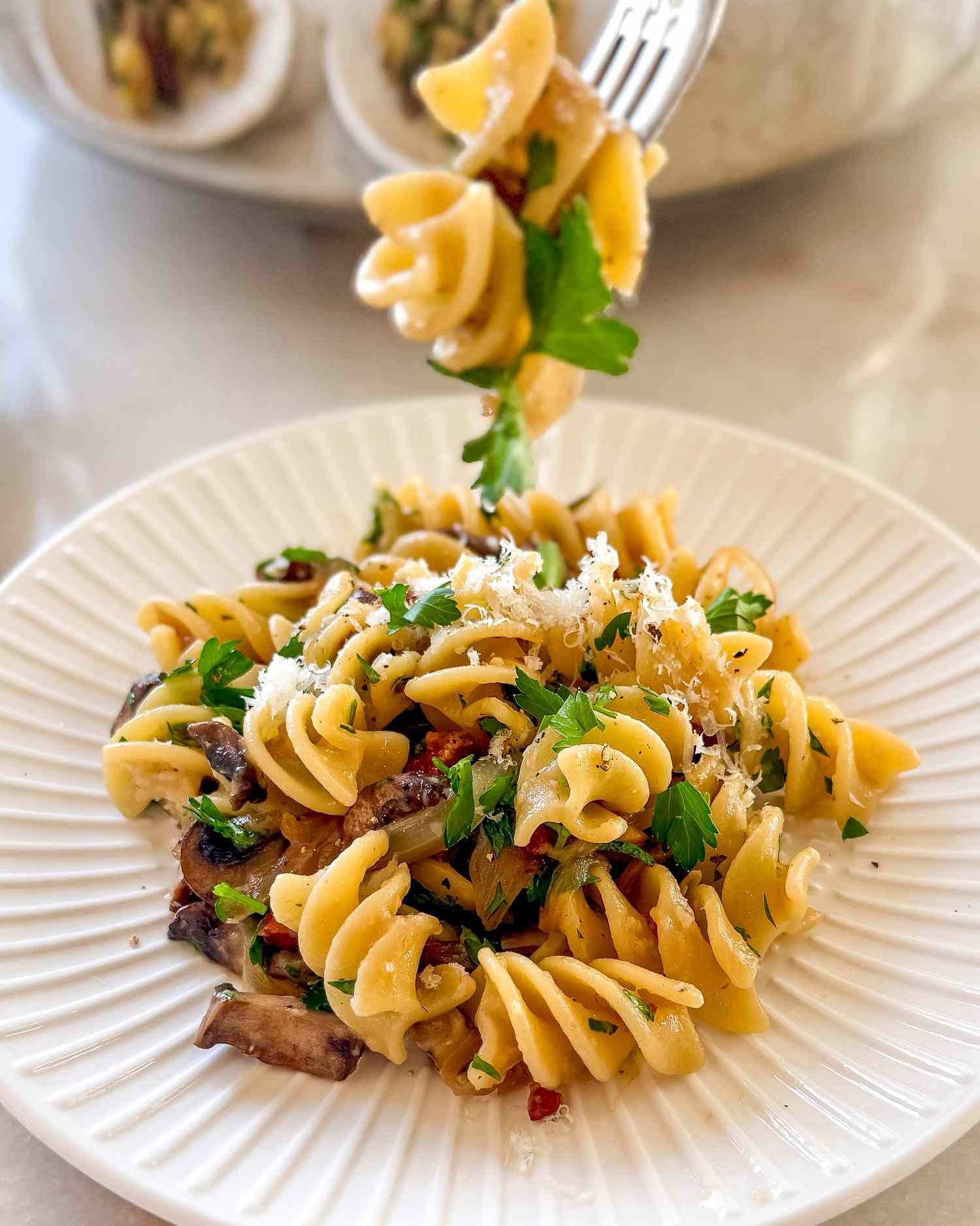 A plate of pasta with mushrooms herbs and grated cheese with a fork serving some from above