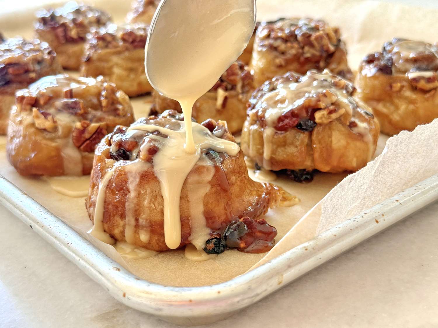 Tray of sticky buns topped with nuts and glaze being drizzled from a spoon