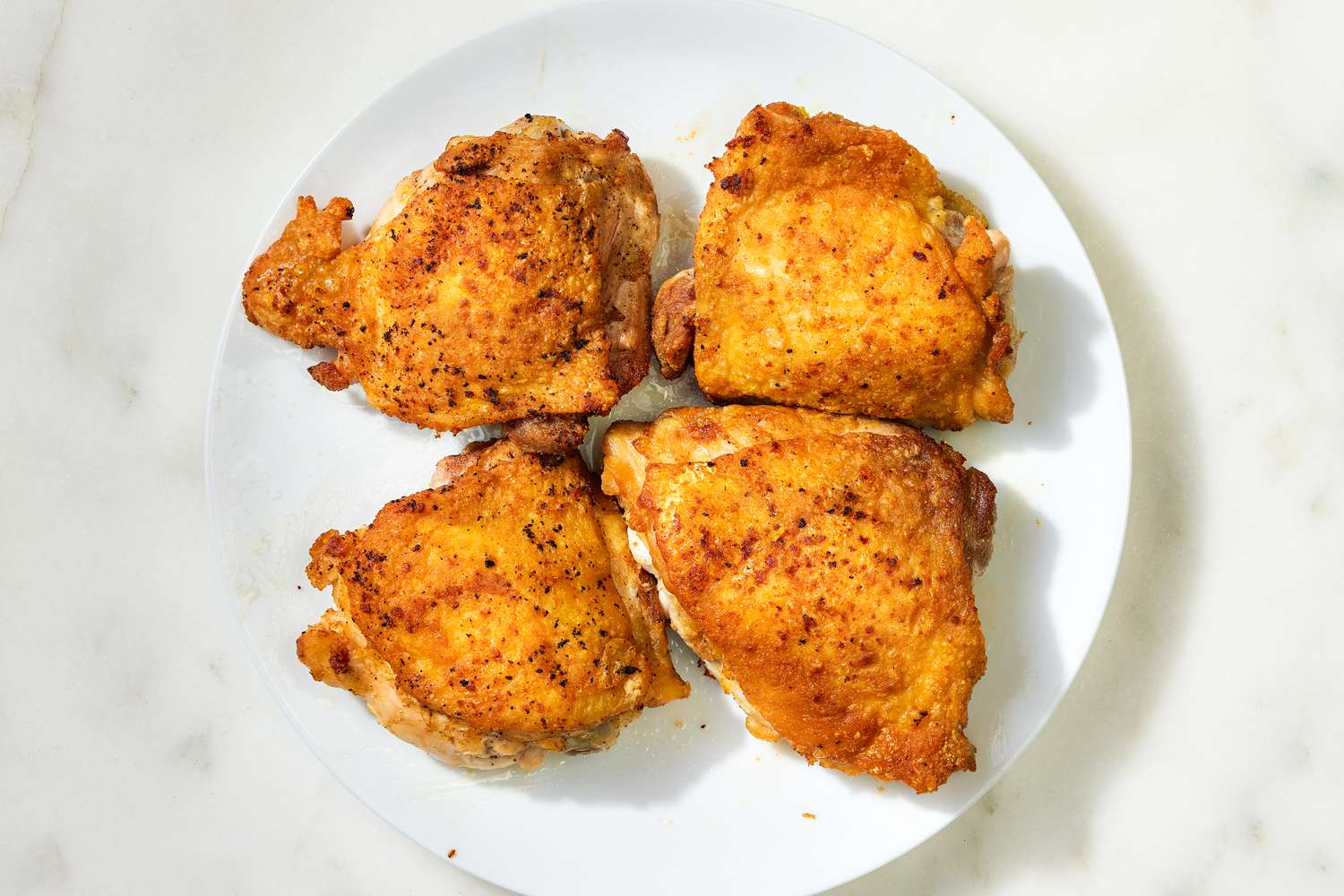 Overhead view of a white plate of four chicken thighs after browning for Country Captain Chicken recipe