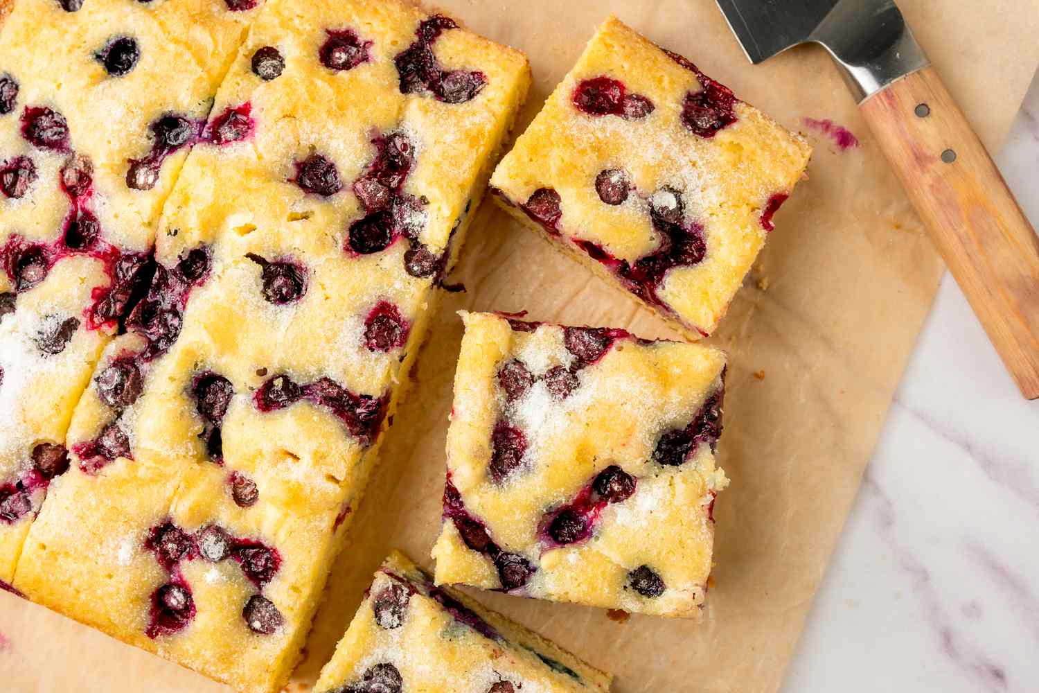 Sliced blueberry sheet cake with a serving spatula on parchment paper