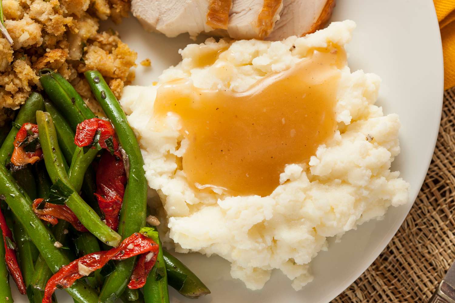 A close-up of a plate with mashed potatoes and gravy, turkey, green beans, and stuffing