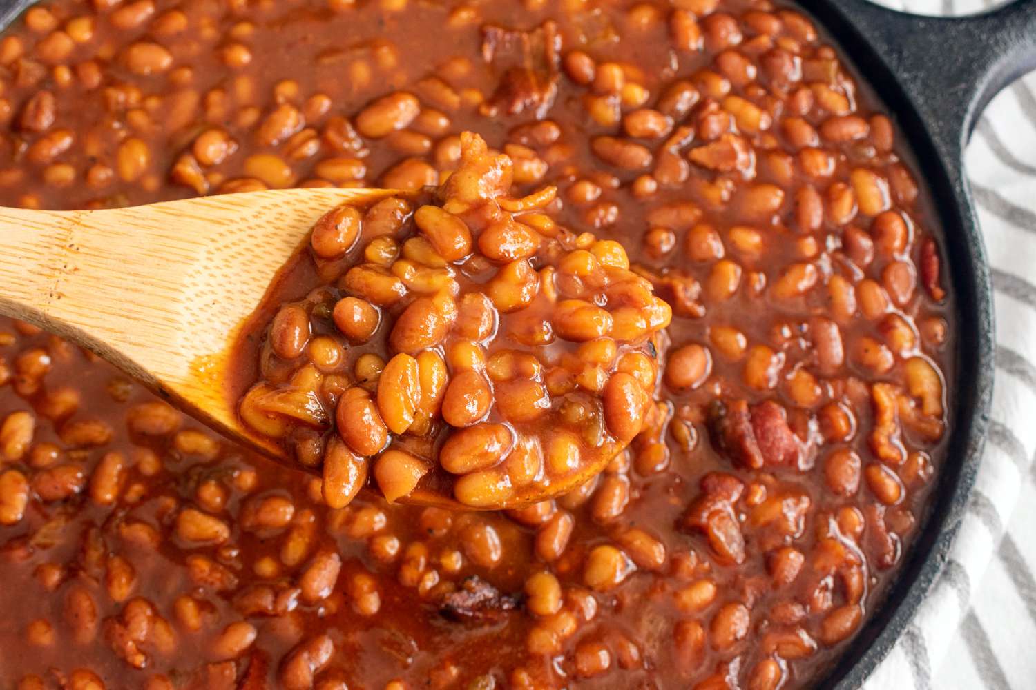 Baked beans in a cast iron skillet with a wooden spoon