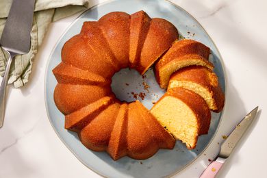 Overhead view of a light blue plate with a partially sliced pound cake next to a cake server and knife on a marble countertop