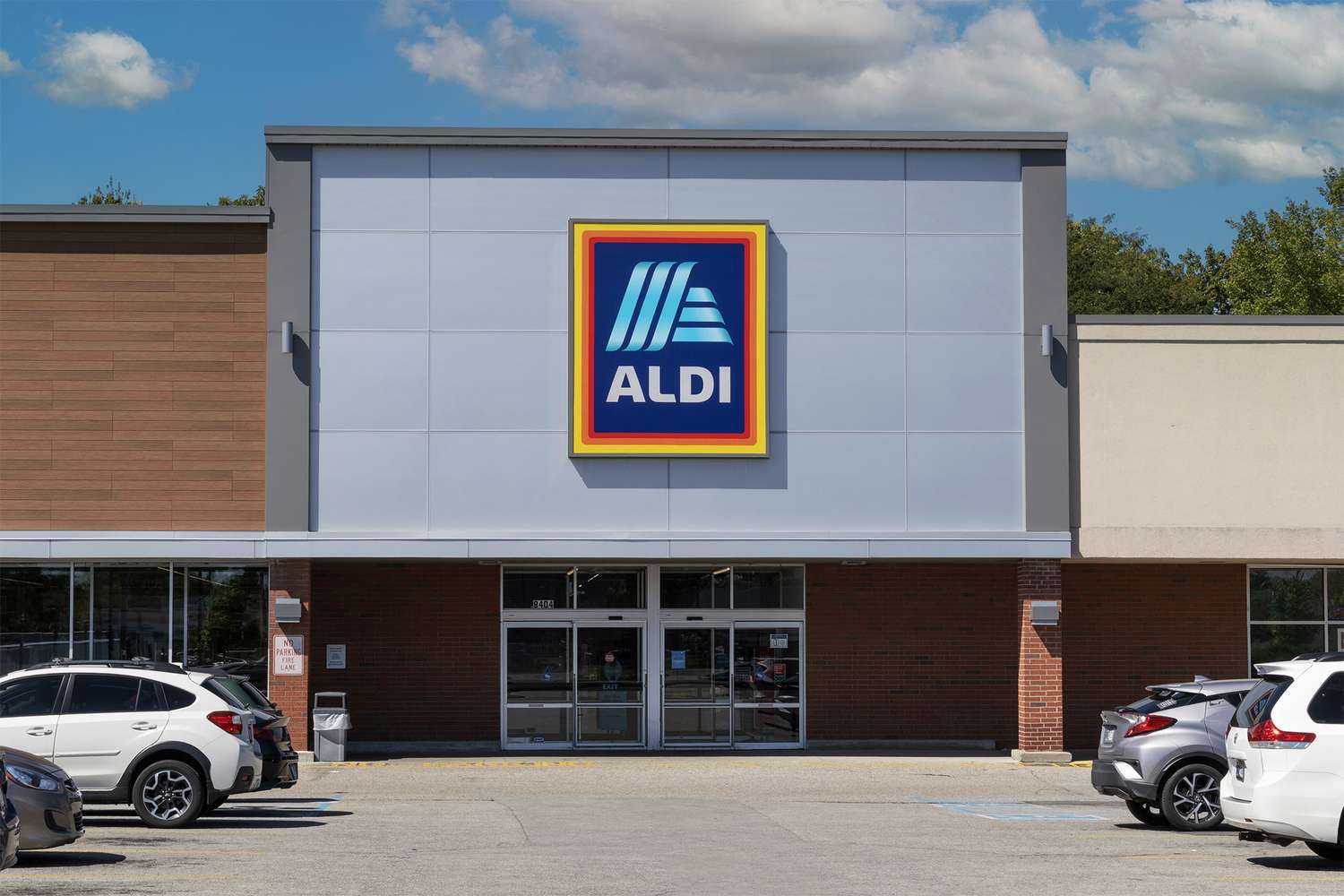 The exterior facade of an Aldi supermarket entrance with parked cars in the foreground