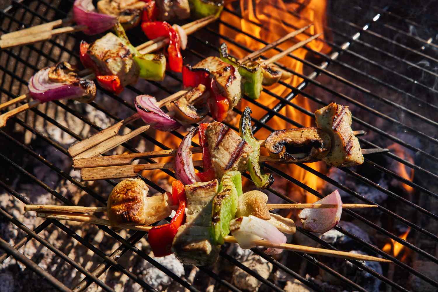 Skewers of grilled vegetables and meat on a barbecue grill over a flame