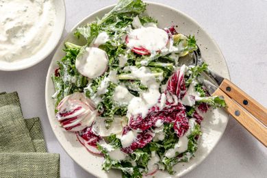 Plate with salad topped with creamy dressing fork and knife on the side napkin nearby
