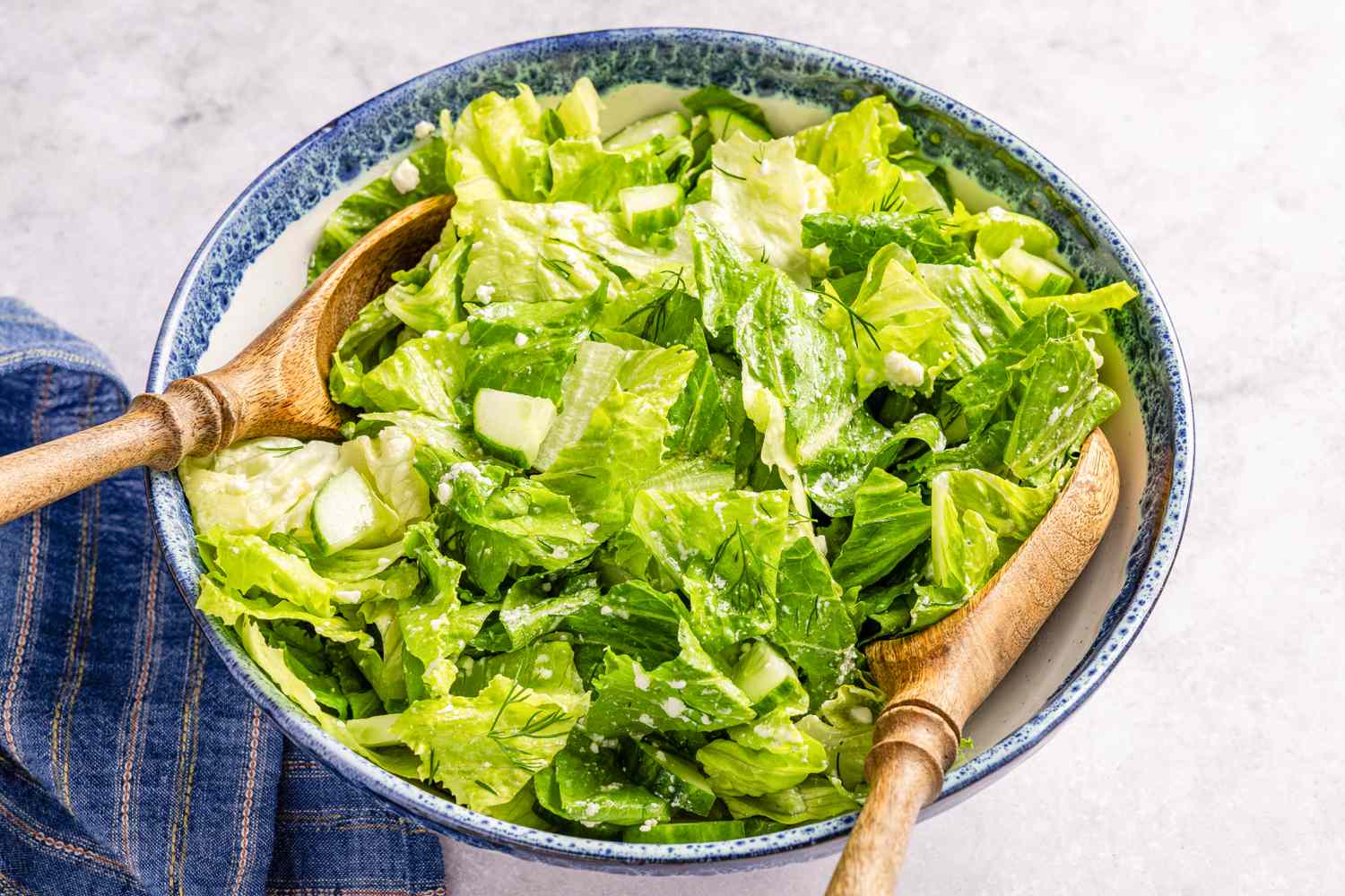 Maroulosalata (greek salad) in a bowl with serving spoons and on the counter next to the bowl, a table napkin